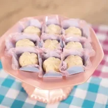Fotografia de brigadeiros de leite ninho em formato de pétalas sobre forminhas azuis e rosa