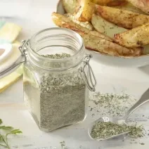 Foto da receita de Sal de Ervas. Observa-se um pote de vidro hermético com o sal dentro e atrás, batatas assadas em um potinho