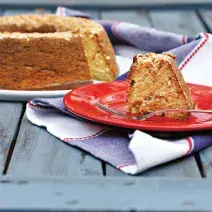 Um prato branco comporta o bolo e um vermelho uma fatia com um garfo. Abaixo um pano nas cores azul e branco.