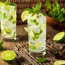 Foto da receita de Mojito Sem Álcool. Observa-se dois copos altos cheio de gelo e hortelã com a bebida dentro, decorado de limões.