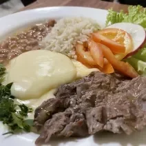 Foto da receita de Purê Francês. Observa-se um prato com um cremoso purê de batatas, acompanhado de arroz, feijão, iscas de carne e uma salada de tomate, rabanete e alface crespa.
