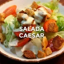 Foto da receita de Salada Caeser. Observa-se um prato com alface americana, tomates cereja, crouton, frango e molho