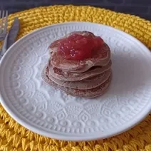 Imagem da receita de Panqueca de batata doce sem glúten com cobertura de geleia de frutas, em um prato branco, sobre uma mesa e ao lado os talheres