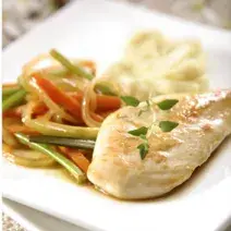 Em um prato quadrado e branco contém um pedaço de frango servido com cenoura, cebola e salsão.