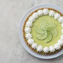 Foto de uma torta limão em cima de um prato branco e com fatias de limão decorando o centro da torta.