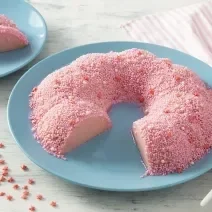 Foto em tons de cor de rosa da receita de pudim rosa servida em uma porção grande com uma fatia cortada sobre pratos de porcelana azul claro