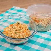 Foto de um pote de vidro redondo e um pote de plástico, ambos com a receita de salada de couscuz marroquino. Os dois estão sobre uma pano azul e branco quadriculado em uma bancada de madeira