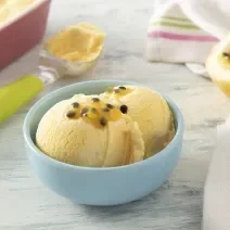 Foto da receita de MOÇA Sorvete de Maracujá. Observa-se um potinho azul com duas bolas de sorvete e um pouco de semente de maracujá por cima.