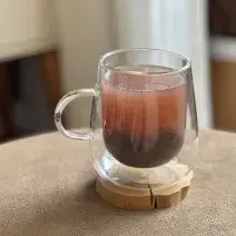 Foto da receita de Bubble Tea Caseiro, servido em uma xícara de vidro transparente, sobre uma pequena base de madeira em uma mesa