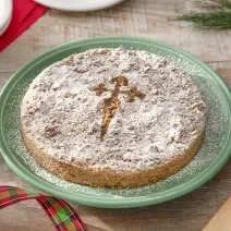 Foto da receita de torta de santiago servida em um prato verde grande sobre uma mesa de madeira com decoração de natal e uma espátula de madeira ao lado