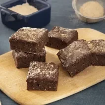 Foto da receita de Brownie com Farinha Láctea NESTLÉ. Observa-se uma tabua de madeira com 6 brownies quadrados com farinha láctea polvilhada