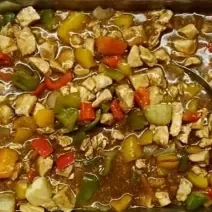 Foto da receita de Frango Xadrez. Observa-se um recipiente refratário com a receita dentro de frango e legumes com molho à base de shoyu.