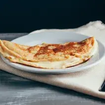 Foto aproximada da receita de Crepioca de Aveia em Flocos, em um prato branco, sobre um tecido em tom bege, com dois talheres de metal ao lado.