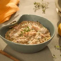 Foto da receita de risoto de salmão com grana padano servida em um bowl de cerâmica azul sobre uma mesa cinza com um limão siciliano cortado ao meio ao lado