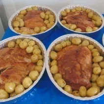 Foto da receita de Pernil Assado com Batatas Coradas. Observa-se 5 travessas de alumínio com o pernil dentro bem dourado e muitas batatinhas ao redor.