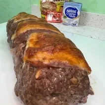 Foto da receita de rocambole de carne moída servida em uma porção grande sobre uma mesa branca