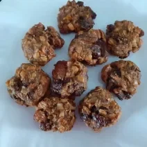 Foto em tons de marrom da receita de cookies de frutas secas e mucilon servida em diversas porções sobre um prato de porcelana branco