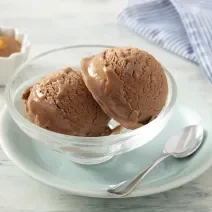 Foto da receita de MOÇA Sorvete de Doce de Leite. Observa-se um potinho individual de vidro com duas bolas de sorvete e, atrás, um potinho com doce de leite cremoso.