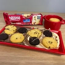 Fotografia de uma barra de chocolate mesclada com chocolate branco, sobre ela uma mistura de biscoitos e cookies.