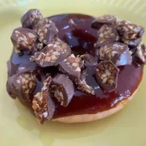 Fotografia de um donuts coberto com caramelo e um pedaço de um bombom de chocolate com caramelo por cima.