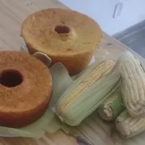 Foto da receita de Bolo de Milho Espetacular. Observa-se dois bolos de milho assados e, ao lado direito, três espigas de milho decorando