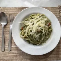 Imagem da receita de Macarrão com Espinafre e Tomate Cereja, em um prato branco e ao lado os talheres