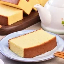 Foto da receita de Bolo Japonês. Observa-se uma fatia de bolo servida em um prato de cerâmica e, ao lado, uma xícara de chá.
