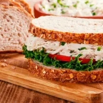 Foto da receita de Sanduíche de Salpicão de Frango. Observa-se um sanduíche bem perto expondo o recheio de frango cremoso com a salada de alface e tomate embaixo.