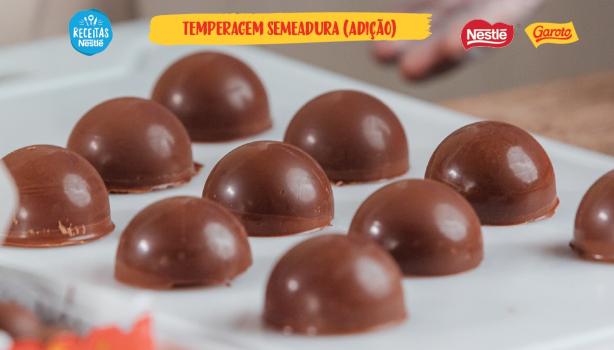 Imagem bastante aproximada de bombons caseiros de chocolate brilhantes sobre papel manteiga com o título do vídeo acima