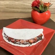 Fotografia em tons de vermelho e marrom com um prato vermelho ao centro. Em cima do prato existe uma receita de tapioca recheada de creme de amendoim e NESCAU Extra Cacau 60%