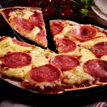 Fotografia em tons de marrom com uma pizza feita com massa de tortilha ao centro. A pizza é feita de queijo, salame e orégano.