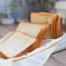 Foto da receita de Pão de Liquidificador sem Sovar. Observa-se um pão cortado em fatias sobre um pano de prato off white.