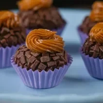 Fotografia de cinco unidades de forminhas azuis com brigadeiro de pão de mel, com doce de leite por cima de cada unidade. Os brigadeiros estão sobre um apoio decorativo de cor azul.