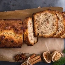 Fotografia vista de cima de um bolo feito em forma retangular, sabor ameixa e chocolate. O bolo está metade cortado em fatias, metade inteiro, sobre um papel manteiga.