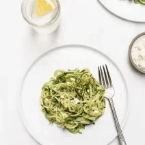 Fotografia em tons claros vista de cima de um macarrão com molho de sálvia, manteiga e vinho, com um garfo ao lado, dentro de um prato branco raso. Ao redor, outro prato com a mesma massa, e, um recipiente pequeno e fundo com molho branco cremoso.