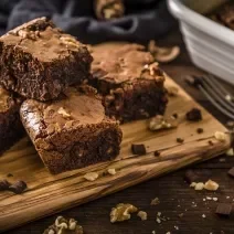 Fotografia de quatro pedaços de brownie feito de farinha de soja, castanha e chocolate. Os pedaços estão sobre uma tábua de madeira perto de um garfo.