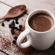 Foto da receita de Chocolate Quente. Observa-se uma xícara branca com a bebida cremosa dentro.