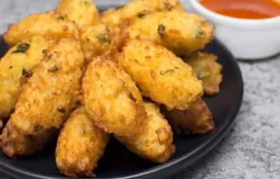 Fotografia de vários bolinhos de couve flor fritos em um prato de vidro preto.