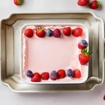 Fotografia vista de cima de um recipiente branco quadrado com uma paleta mexicana de travessa, com morangos por cima, dentro de uma forma de alumínio.