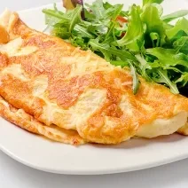 Foto aproximada de uma omelete dobrada ao meio e servida com algumas folhas verdes em um prato. Esta omelete foi prepara na airfryer de acordo com a receita.