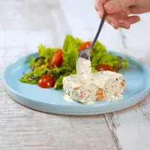 Fotografia em tons de branco e azul de uma bancada branca, sobre ela um prato redondo azul com salão e salada.