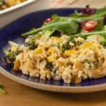 Fotografia em tons de marrom e azul de uma bancada de madeira, sobre ela um prato redondo azul com arroz e salada de folhas. Ao fundo um recipiente branco.