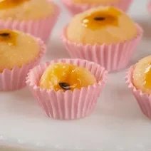 Fotografia em tons de rosa com várias forminhas de brigadeiro ao centro. Dentro de cada forminha existe brigadeiros feitos de maracujá finalizados com geleia de maracujá no topo.