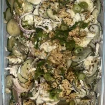 Fotografia em tons de verde com uma travessa de vidro ao centro. Dentro da travessa existe uma salada de pepino com cebola roxa e cream cheese