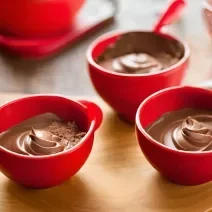 Fotografia em tons de vermelho com três potes vermelhos ao centro. Dentro de cada pote existe uma mousse de chocolate cremosa feita com NINHO Primeira Infância