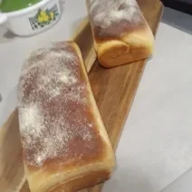 Fotografia de dois pães grandes de milho sobre uma tábua retangular de madeira.