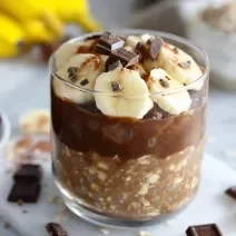 Fotografia em tons de amarelo com um copo de vidro ao centro. Dentro do copo existe uma receita de Overnight Oats com Banana e NINHO Adulto