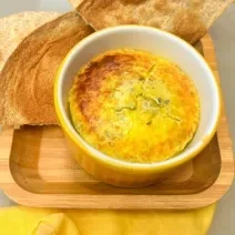 Fotografia em tons de amarelo com um ramekin amarelo ao centro. Dentro dele existe uma receita de ovos cremosos acompanhado de pão.