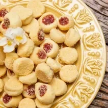 Fotografia de um prato amarelo de vidro sobre uma mesa de madeira. Dentro do prato tem várias unidades de biscoitos amanteigados com goiabada.