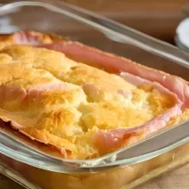 Fotografia mostra a uma torta salgada dourada com fatias destacando o recheio colorido de presunto